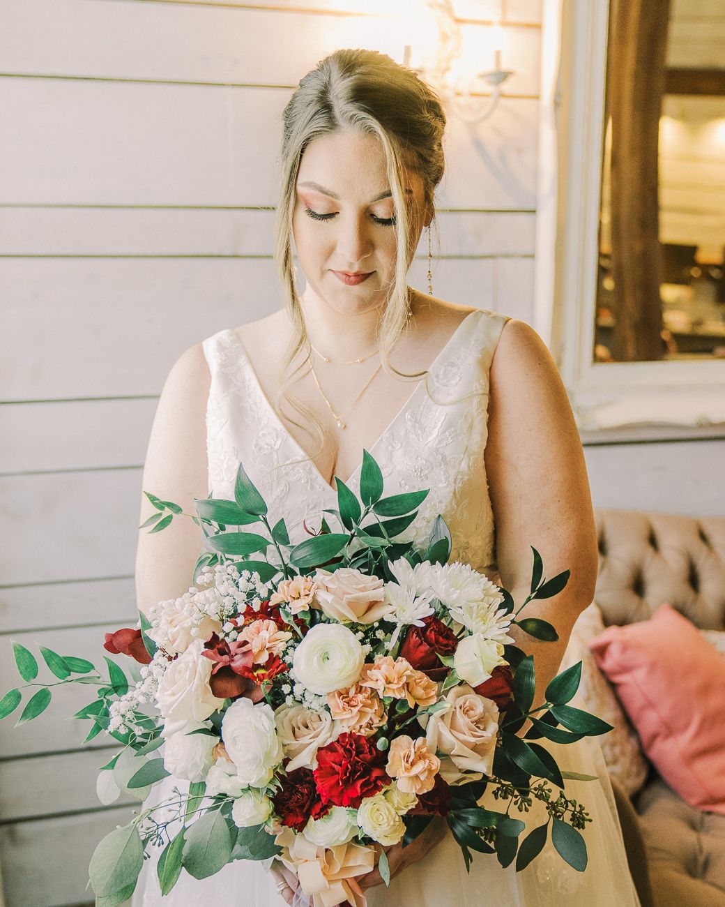 A stunning bridal bouquet featuring red, white and peach roses with green foliage held against a lace wedding dress.