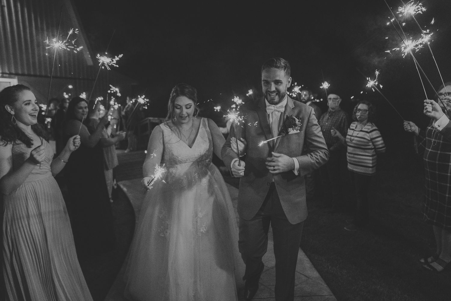 Wedding guests hold sparklers in the dark during an outdoor nighttime celebration creating a magical atmosphere.