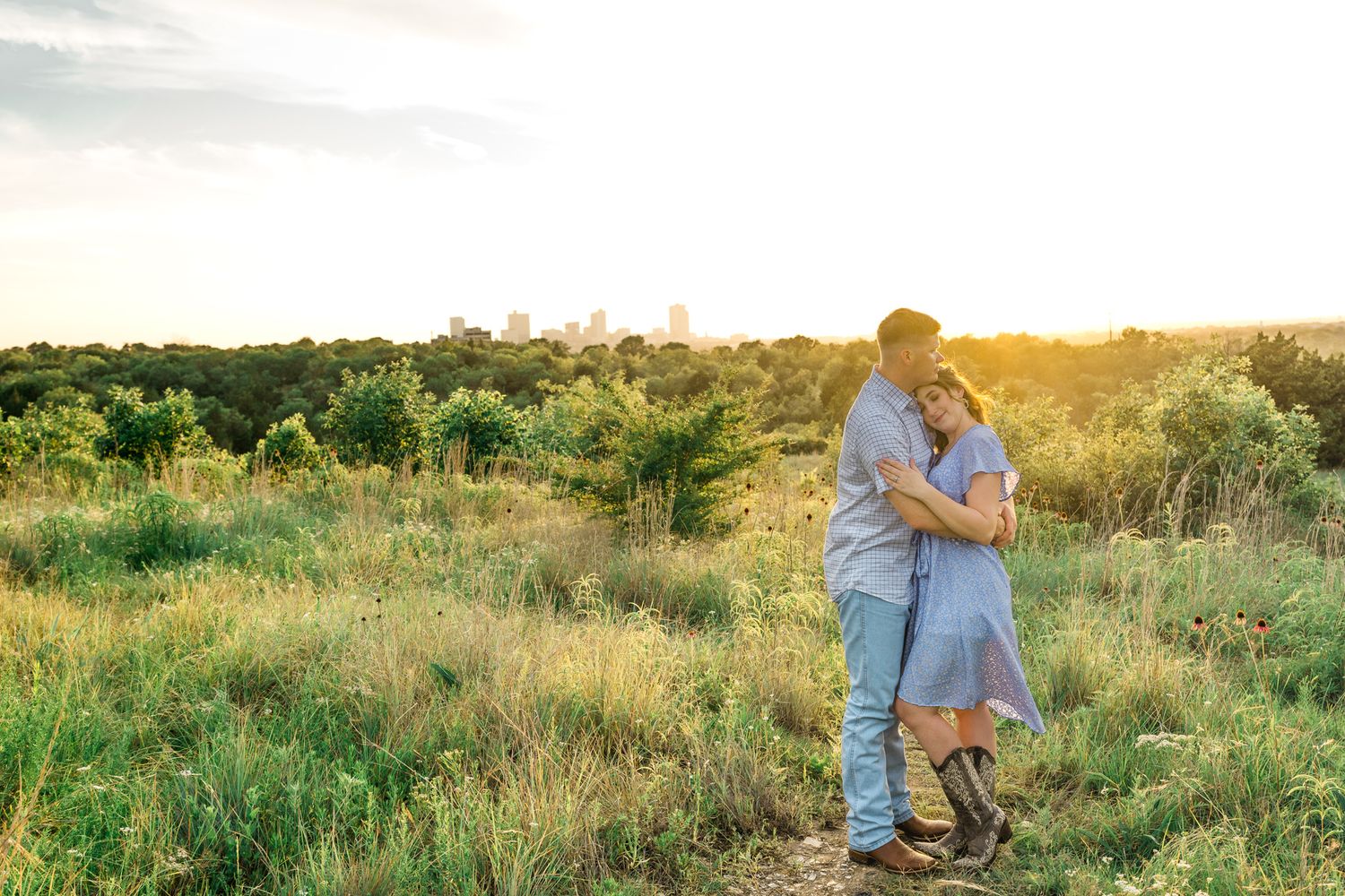 A loving couple stands together in a sunlit field of tall grass during a summer evening.