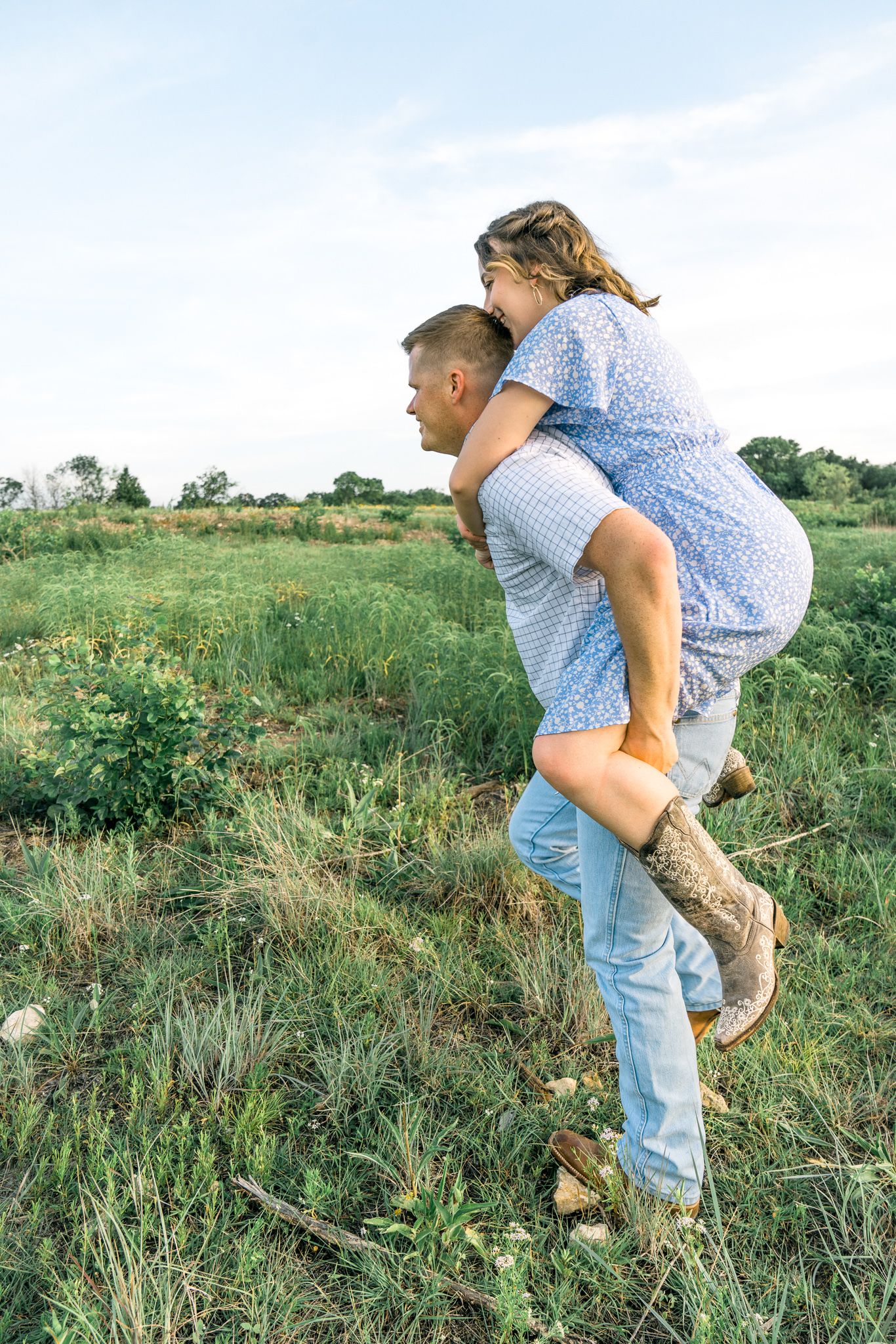A playful scene unfolds in a grassy field as two people engage in a lighthearted chase through tall grass.
