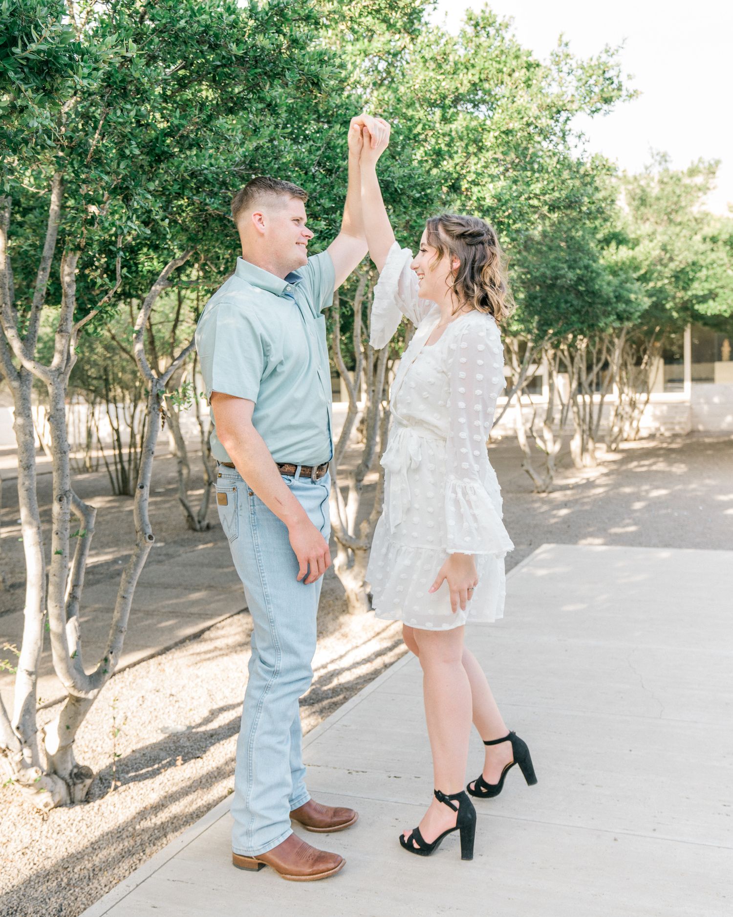 Couple in coordinated blue and white outfits dancing together in a sun-dappled outdoor setting.
