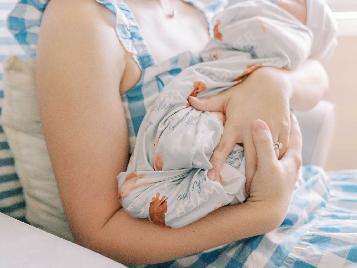 A parent holds their sleeping newborn baby wrapped in a white swaddle blanket against a soft blue background.