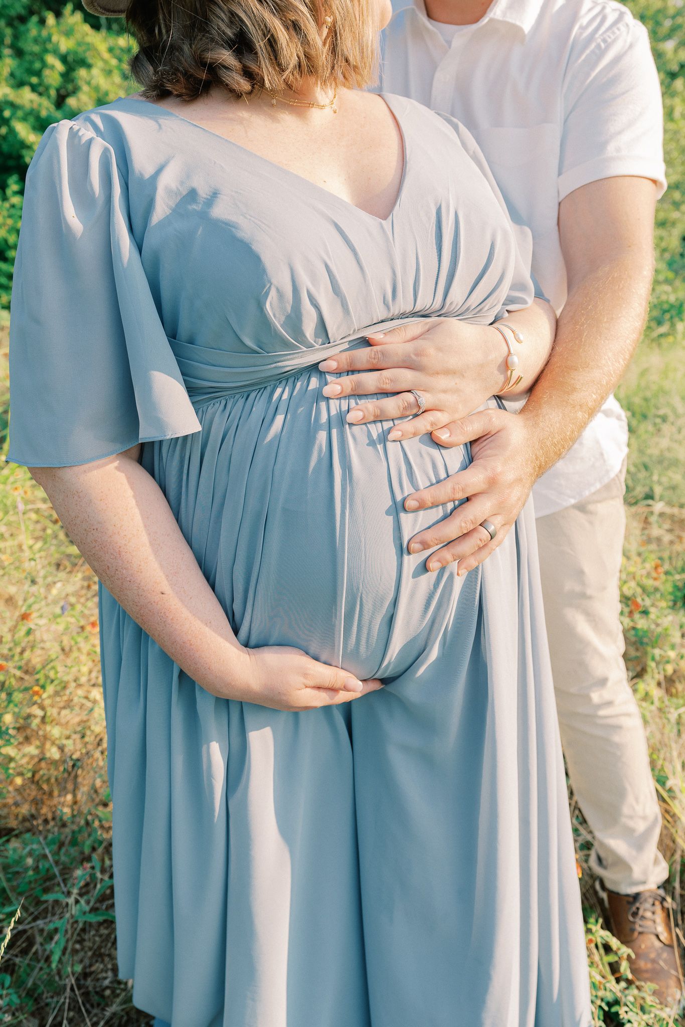 A series of photos showing hands cradling a pregnant belly in a light blue empire waist dress against a natural outdoor setting.