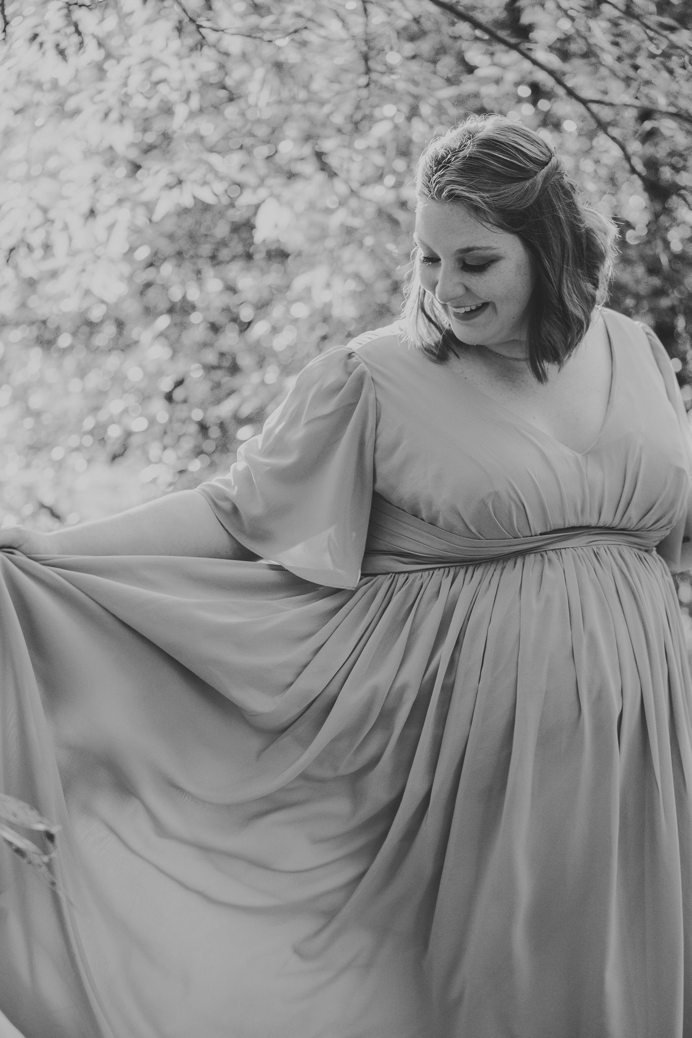 A person wearing a flowing white maternity dress twirls in a series of graceful poses against a light background.