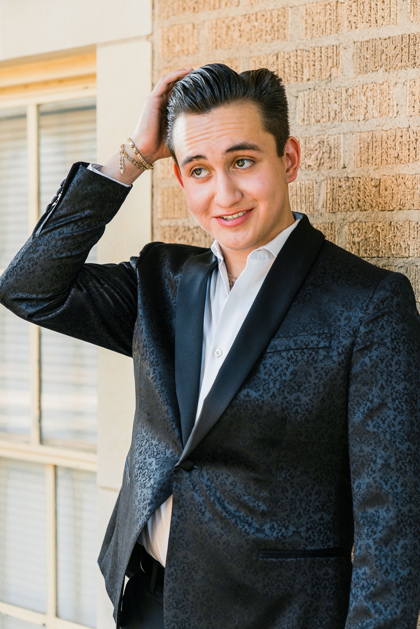 Professional portrait of someone in a dark suit jacket against a brick wall with a casual pose.