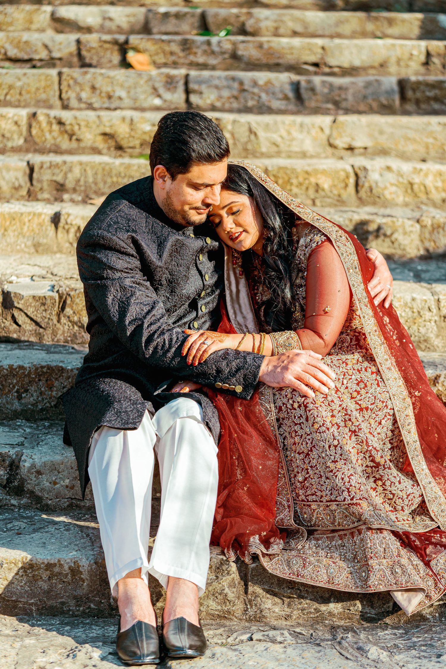 A couple in traditional attire shares an intimate moment sitting on stone steps at sunset.