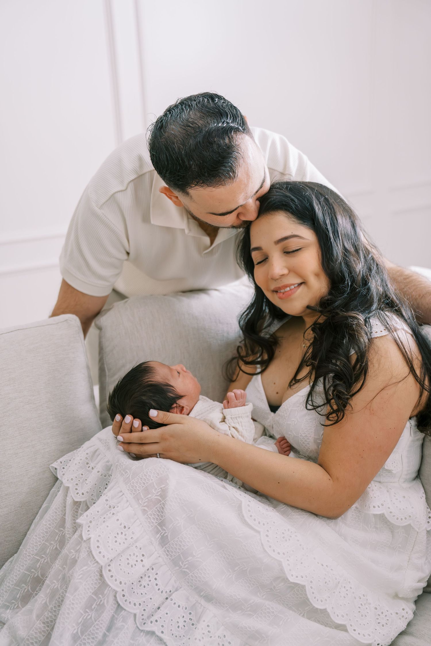 A couple in white outfits lovingly gazes at their newborn baby during a professional newborn photography session.