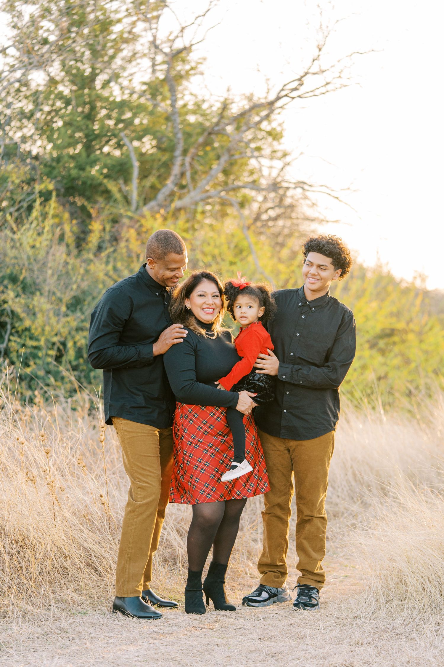 A family shares joyful moments together in a sunlit field with tall grass during an outdoor photo session.