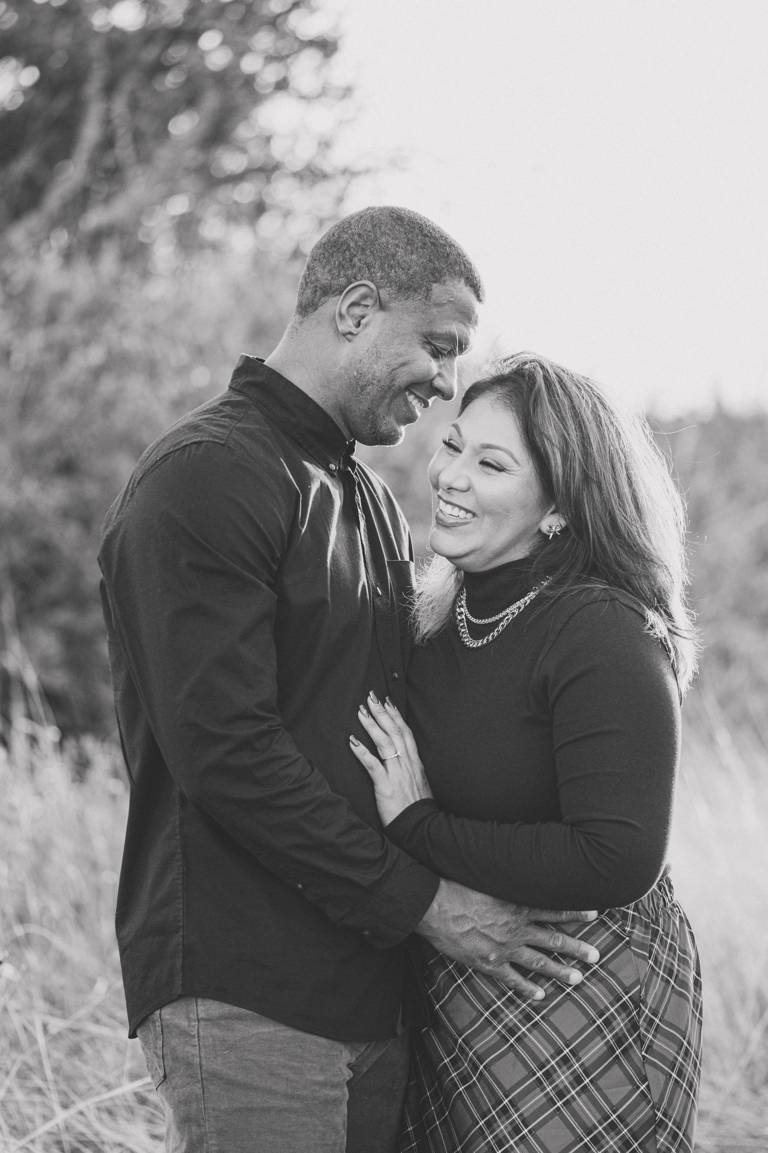 A romantic black and white portrait of a couple embracing and laughing together outdoors.