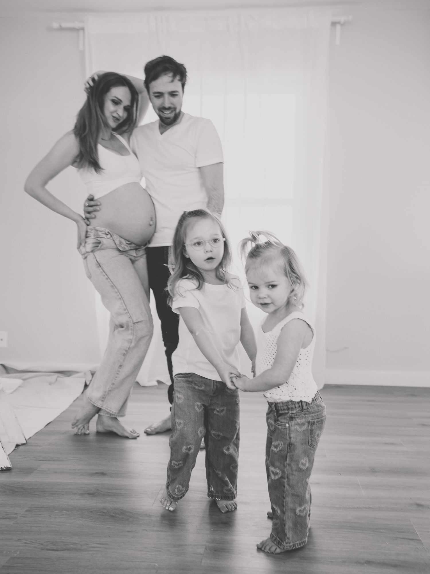 Black and white maternity photo with children playing in foreground.