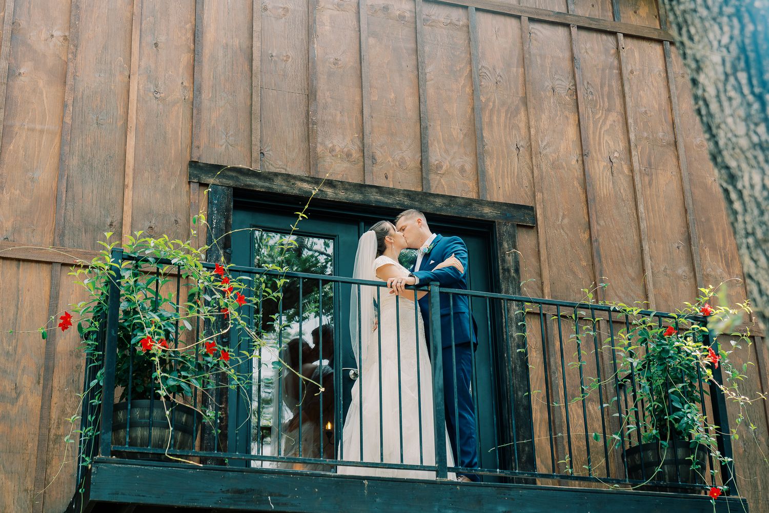 A couple shares an intimate moment on a rustic wooden balcony adorned with flowering vines.