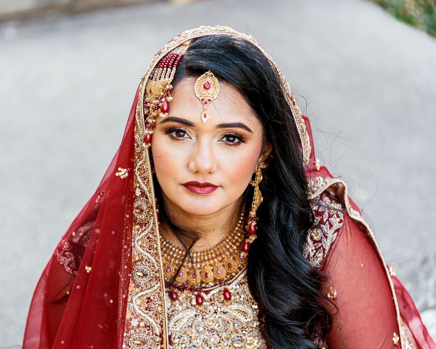 A bride in a red and gold embroidered lehenga and traditional Indian bridal jewelry poses for portraits.