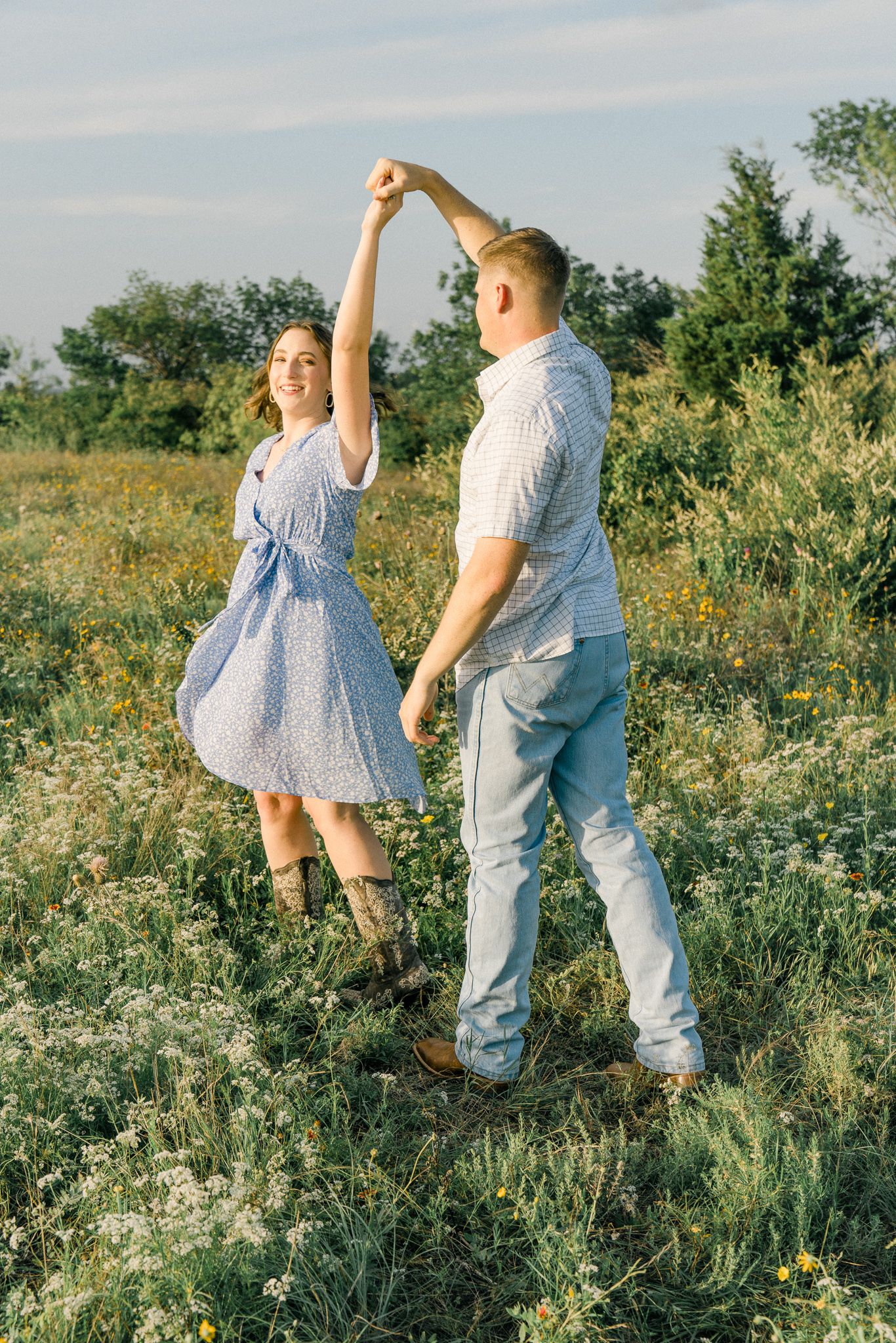 Two people share a playful dance among blooming wildflowers in a sunny field.