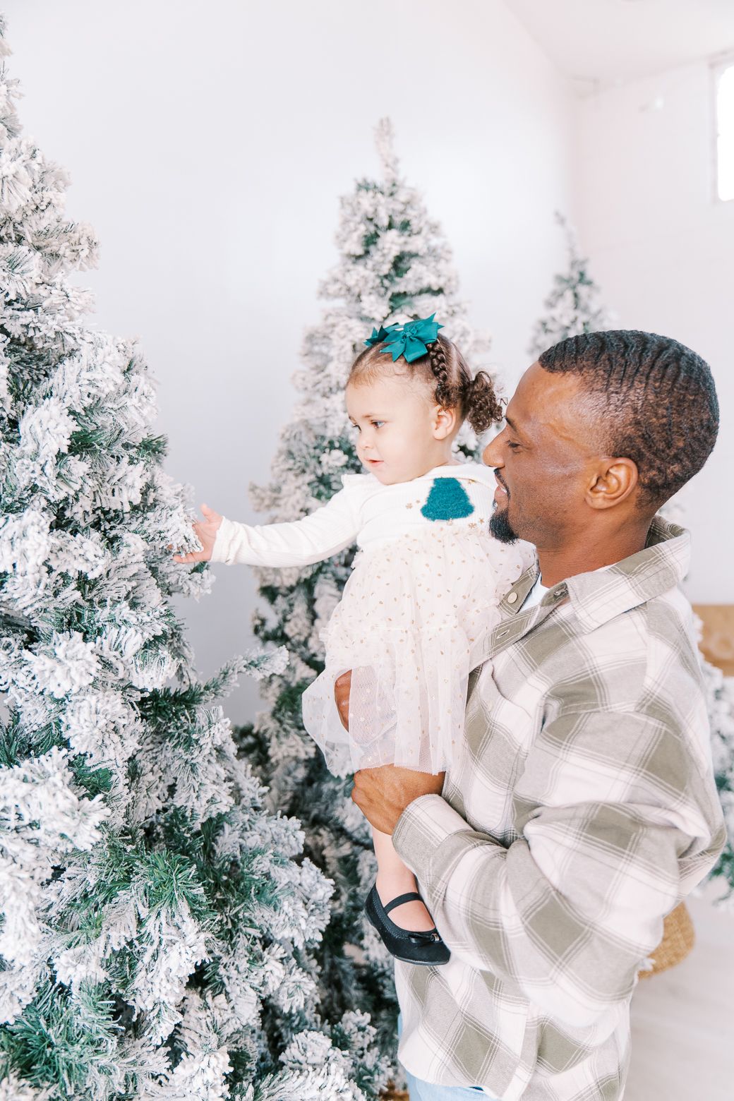 Playful winter portrait session with flocked Christmas trees and white plaid shirt.