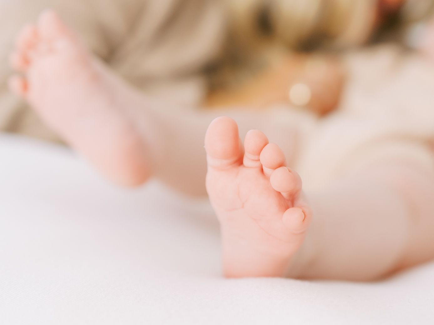 A baby's tiny feet and toes are gently held in adult hands against a soft white background.