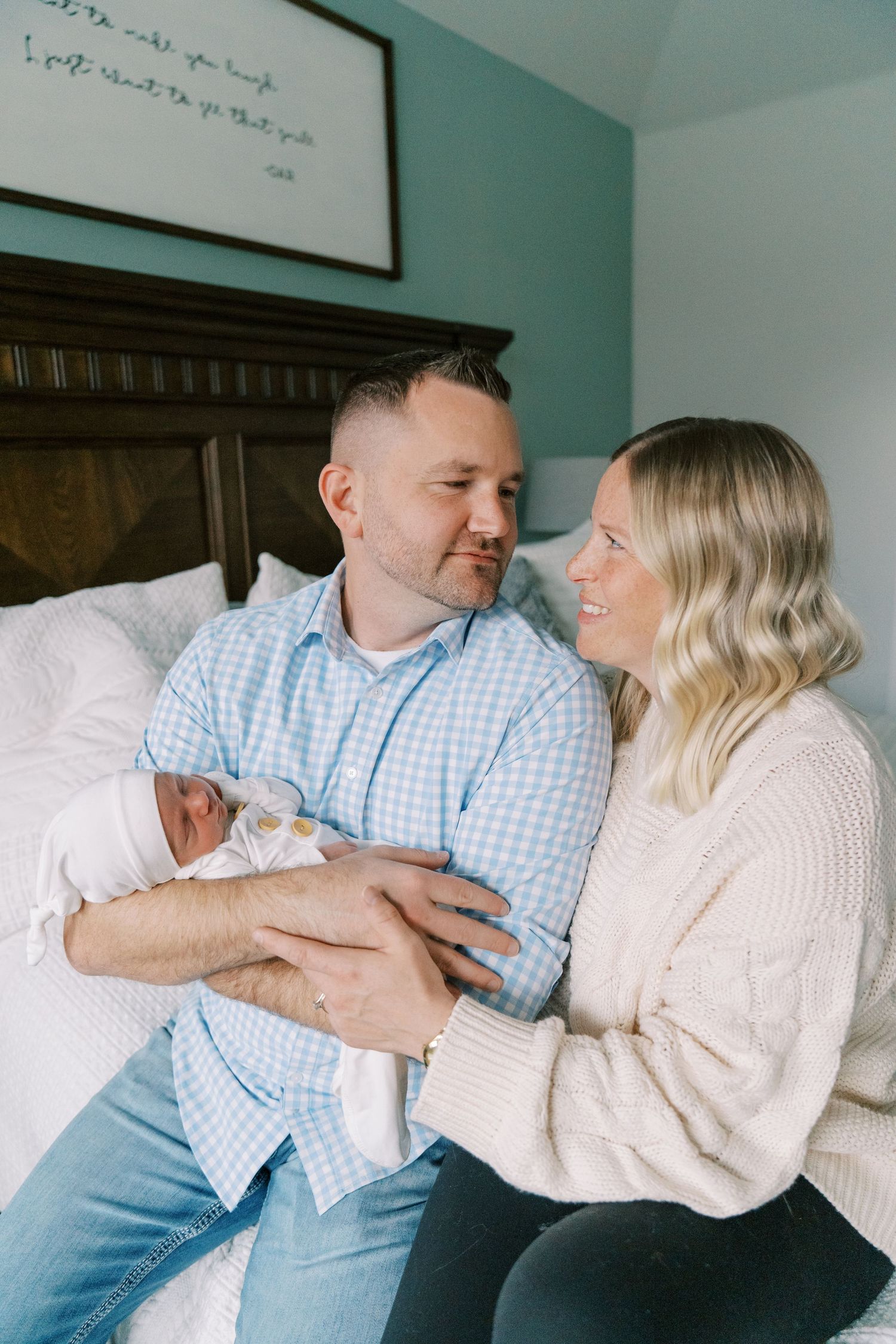 Couple laughs together while cuddling with their newborn on bed.