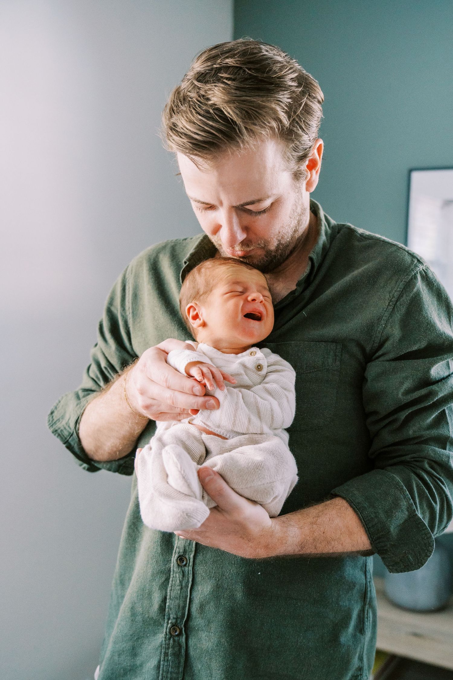 Parent in dark green shirt comforts crying baby wearing white onesie in series of tender moments.