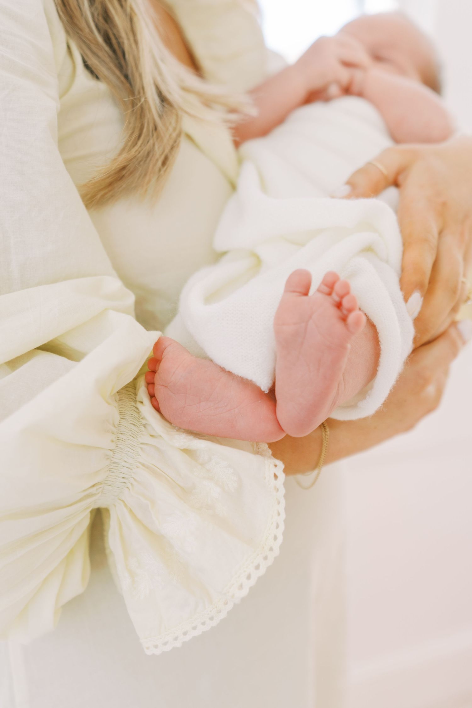 Baby's tiny feet peeking out from white clothing while being cradled.