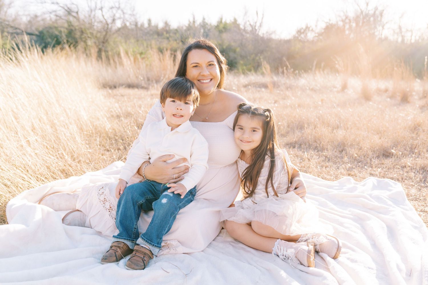 Family enjoying quality time together on a white blanket in a sun-drenched field during golden hour.
