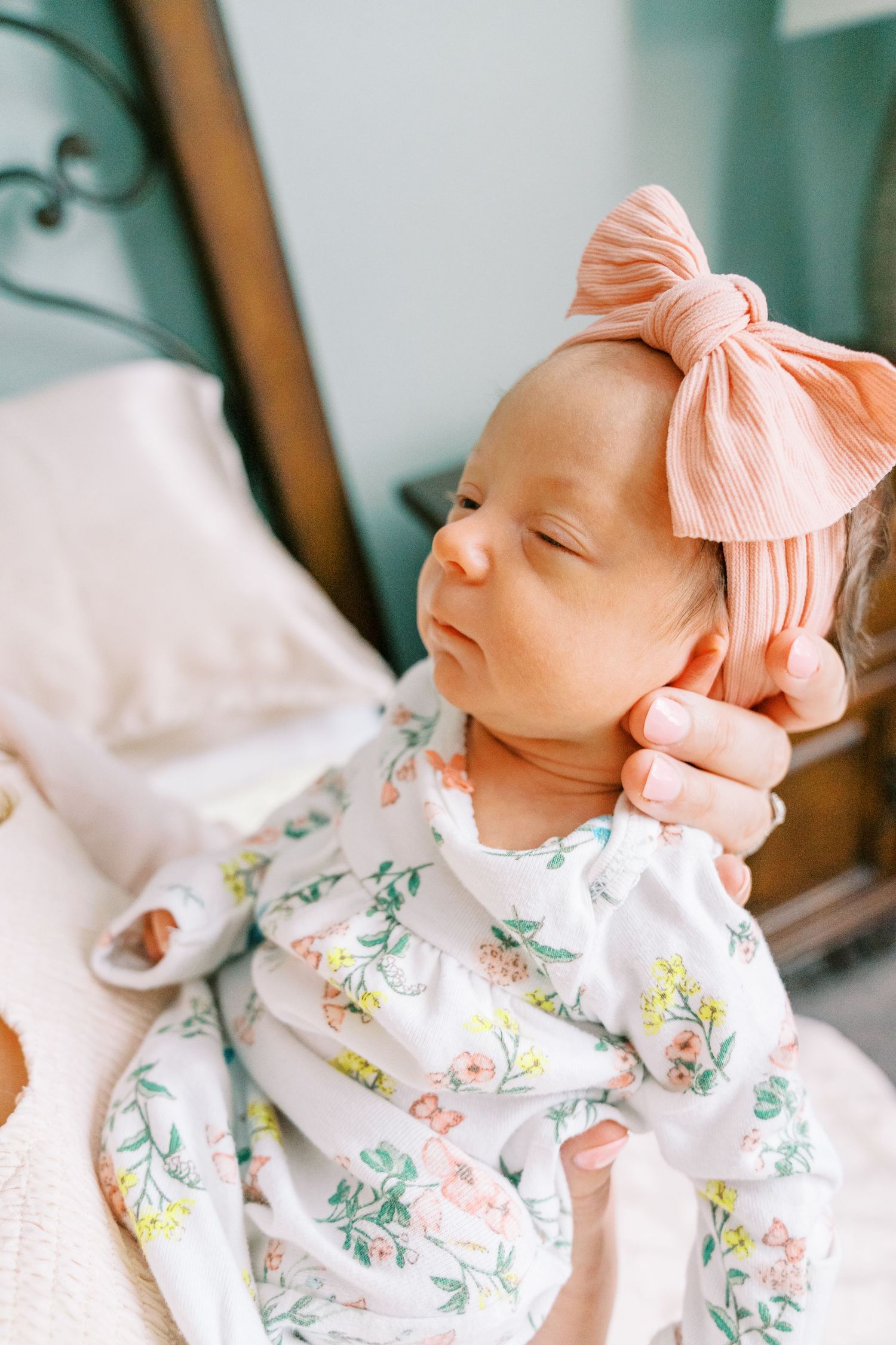 Sleeping newborn wearing floral outfit and pink bow headband in natural light.