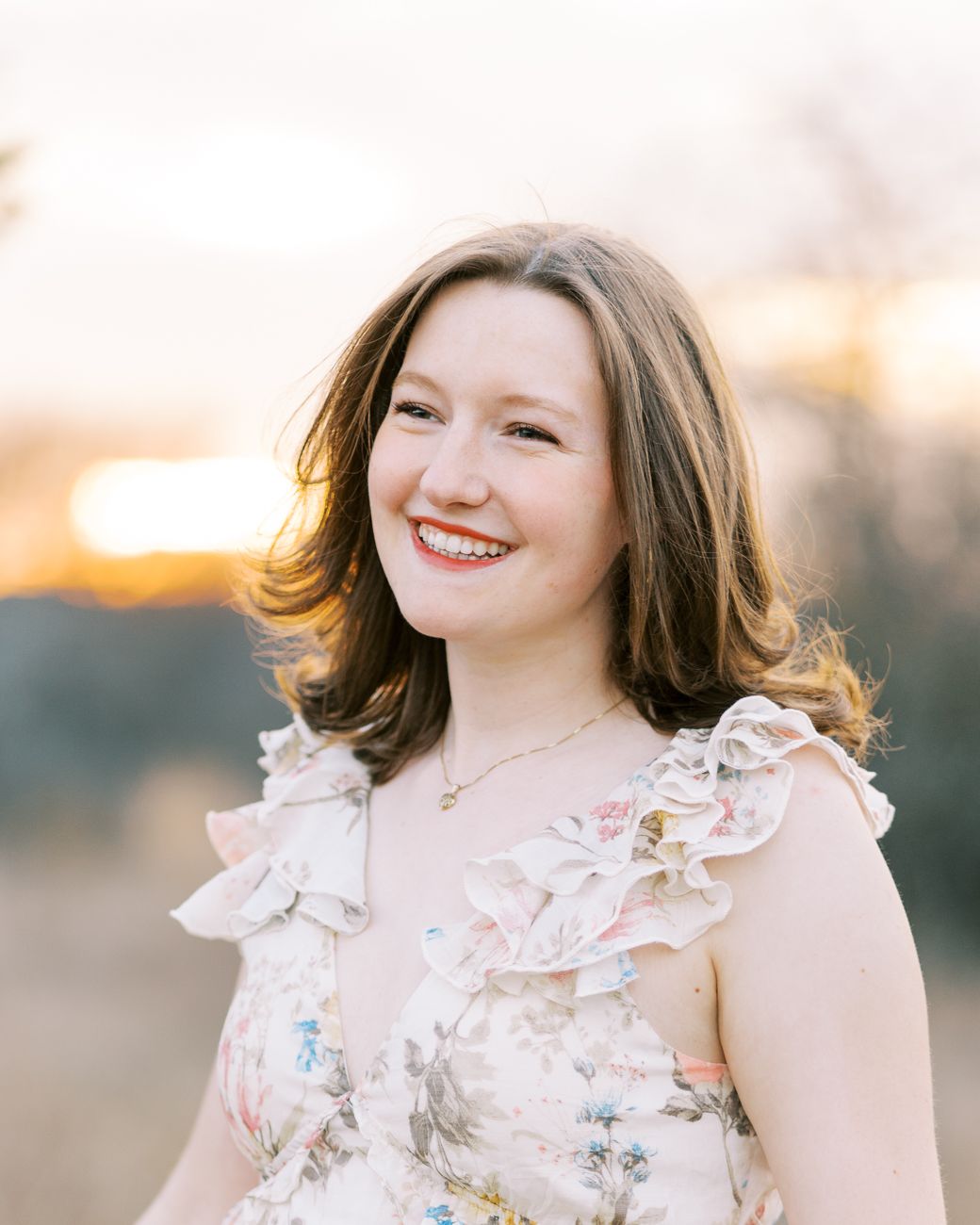Outdoor portrait with warm golden lighting showing floral dress and soft styling.