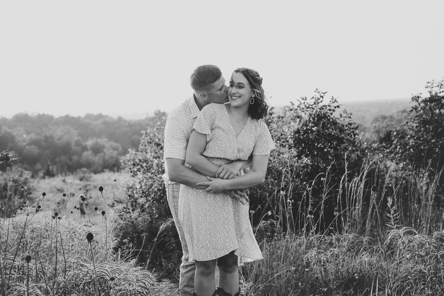 Black and white romantic portrait in a scenic hillside setting.