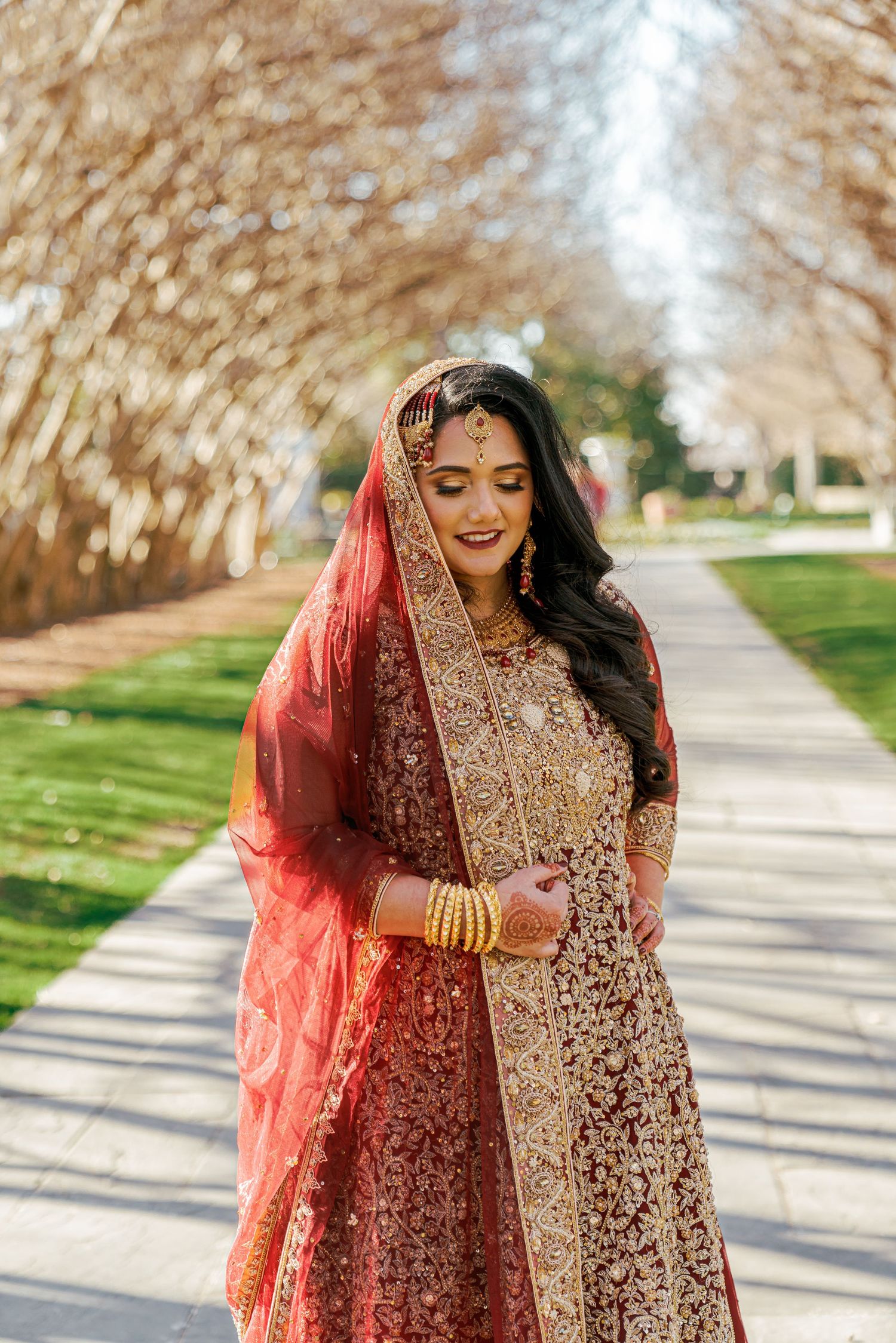 Person in ornate red and gold traditional dress walking along a tree-lined pathway.