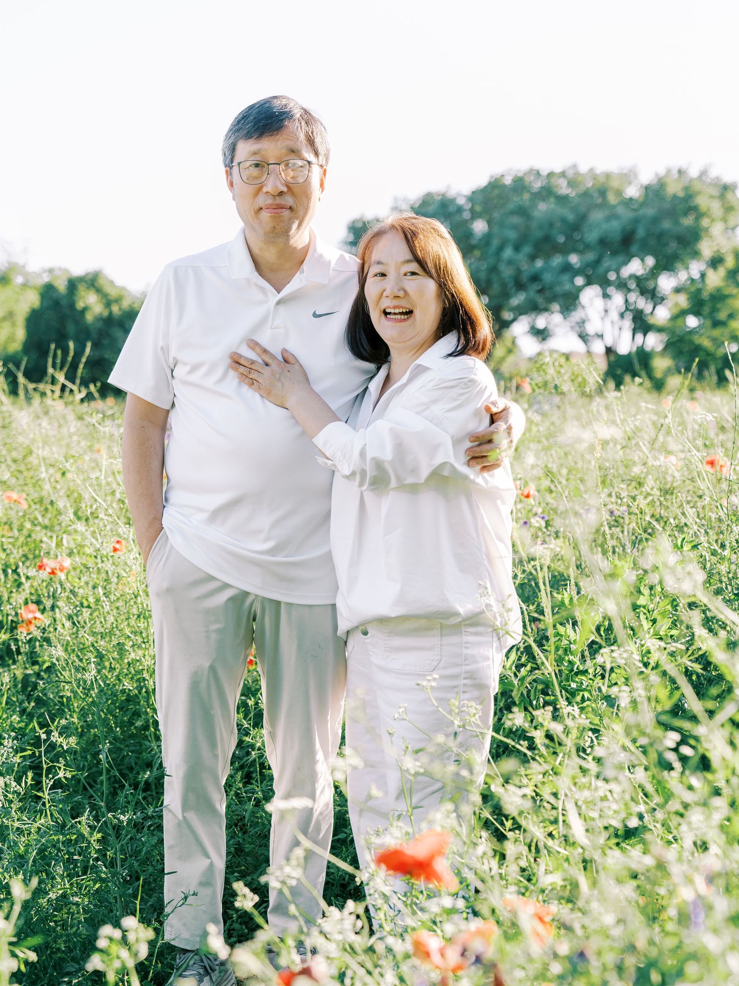 A couple wearing all white outfits share joyful moments together in a sunny wildflower meadow.