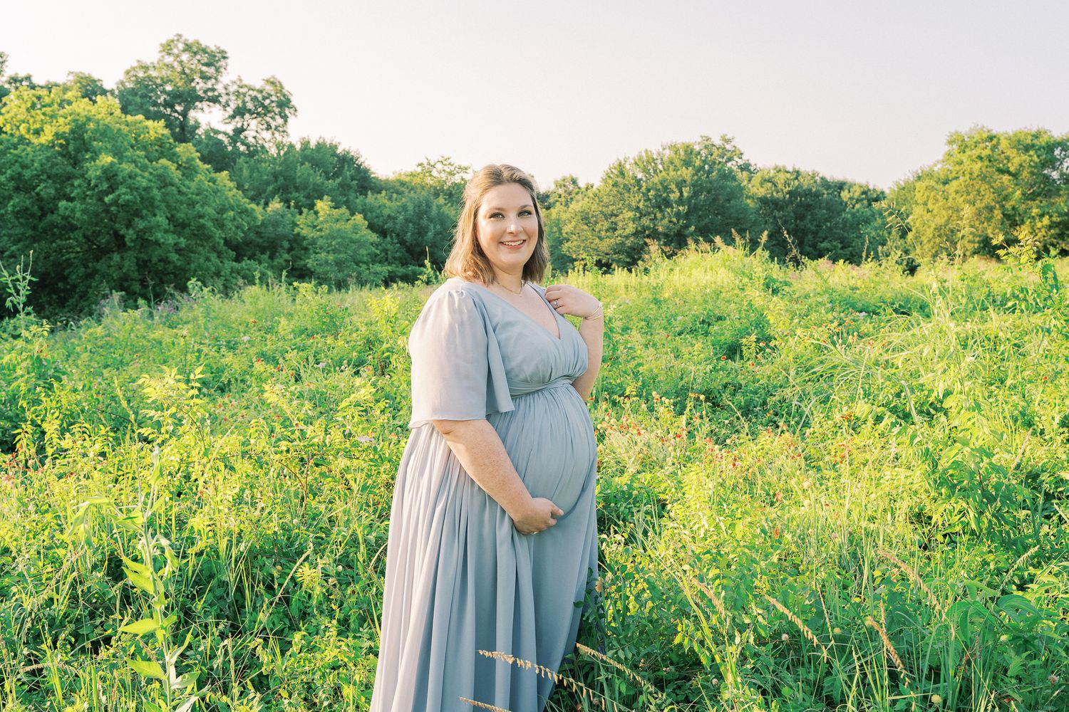 A couple shares a tender moment while standing in a lush green field at sunset.