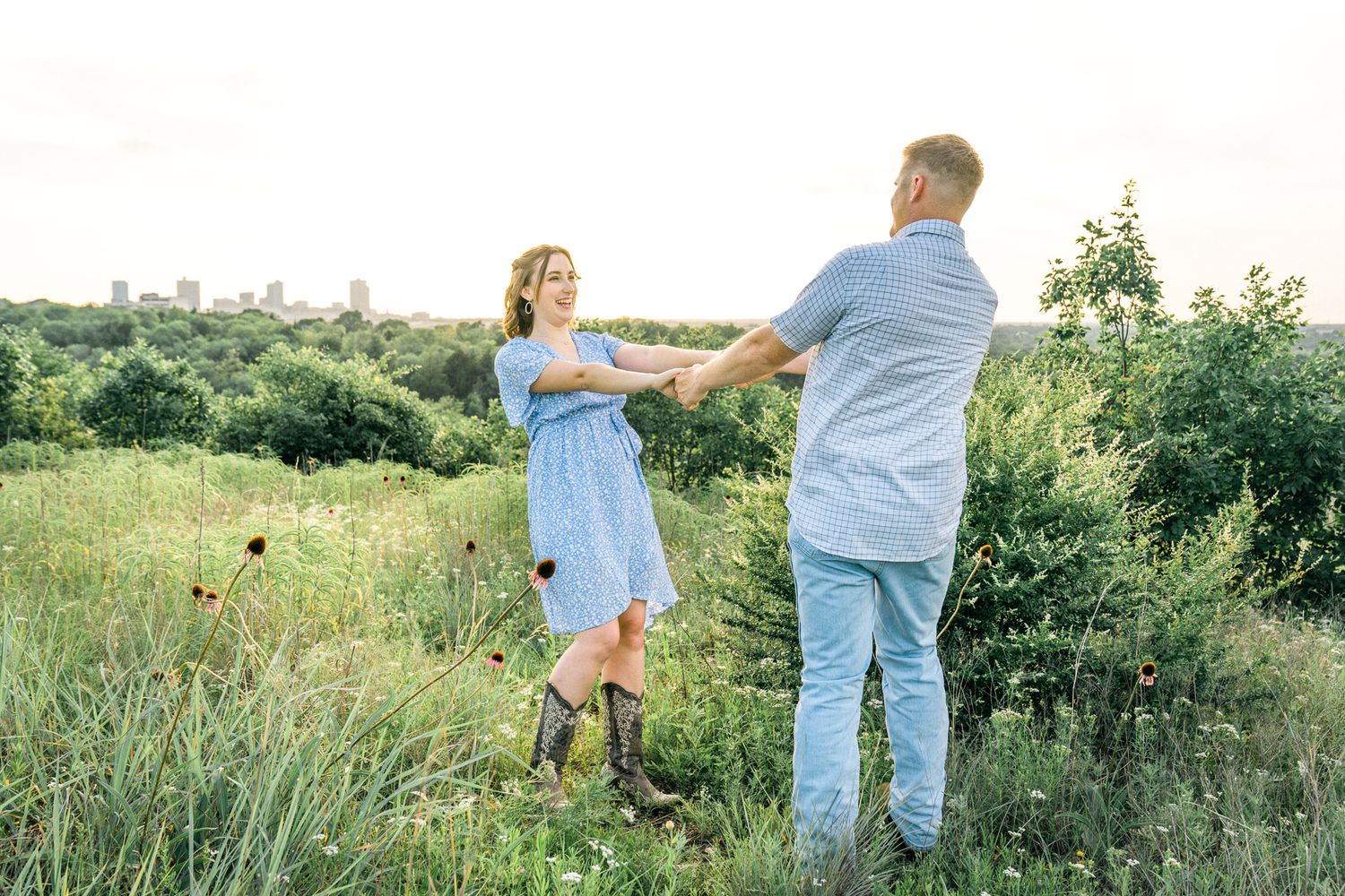 A couple dances together in a wildflower field with a distant cityscape visible behind them.