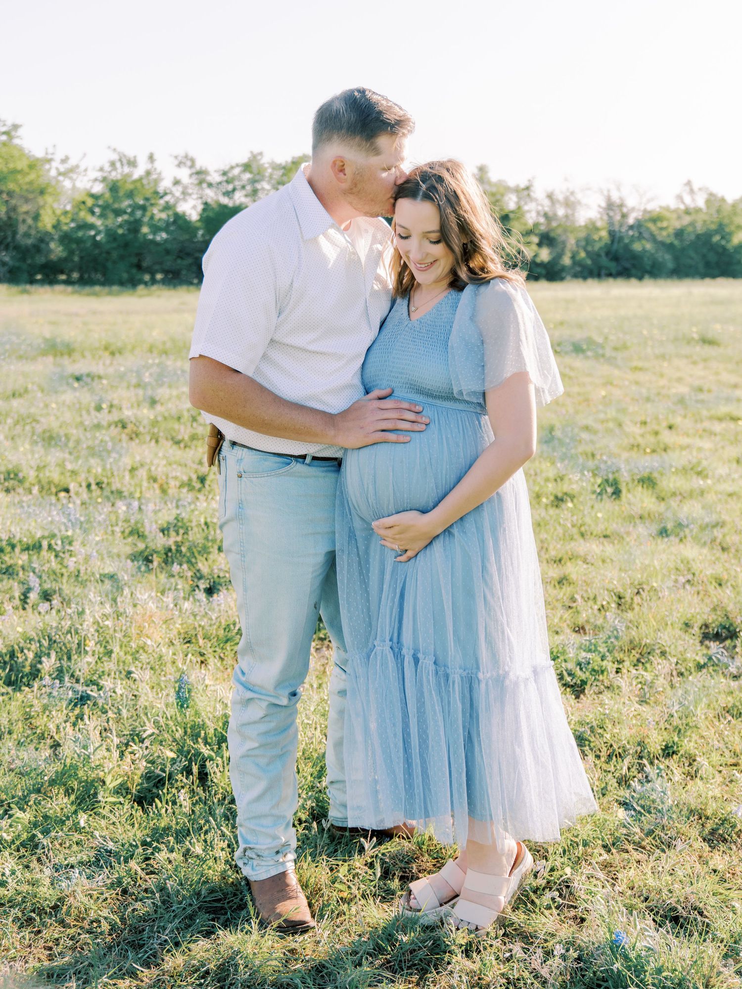 A couple poses together in a sunlit field during their maternity photoshoot.