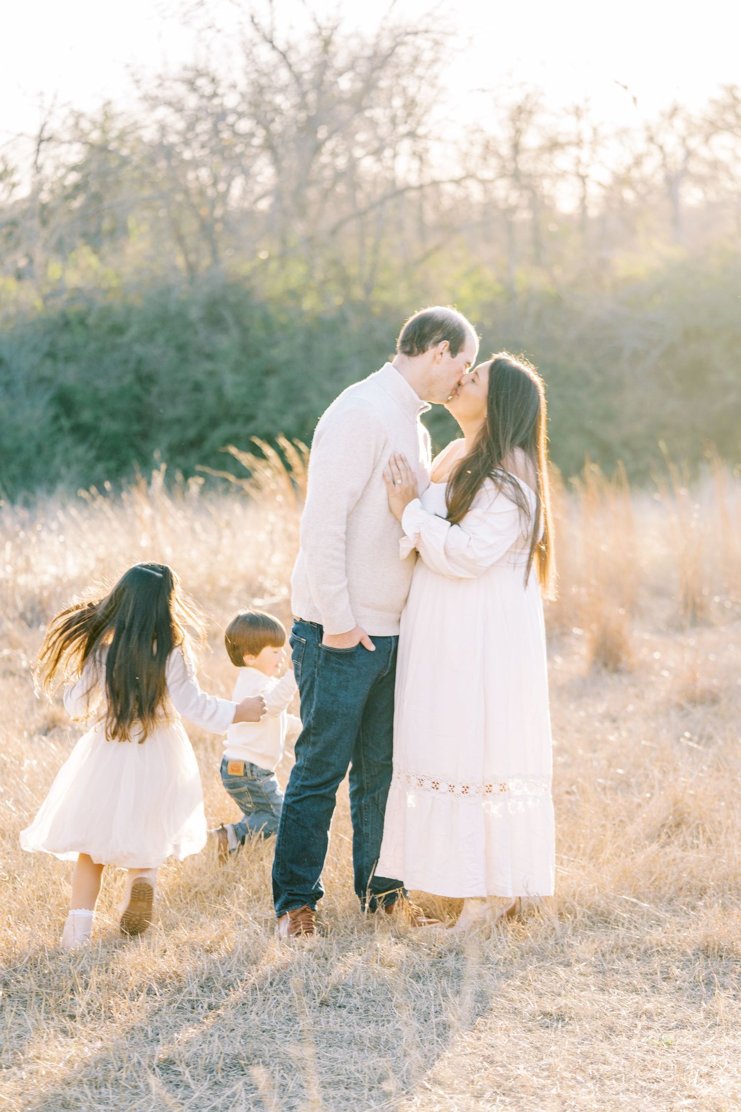 A tender family moment captured in a sun-drenched field with tall grass during a photo session.