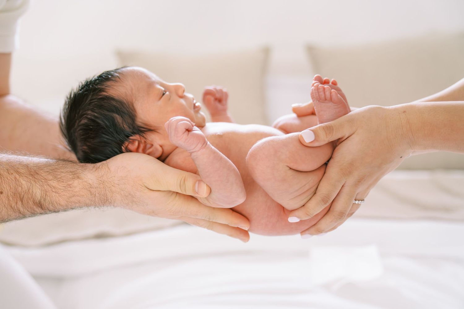 Two parents gently cradling their newborn baby on a white bed, showing tender family bonding moments.