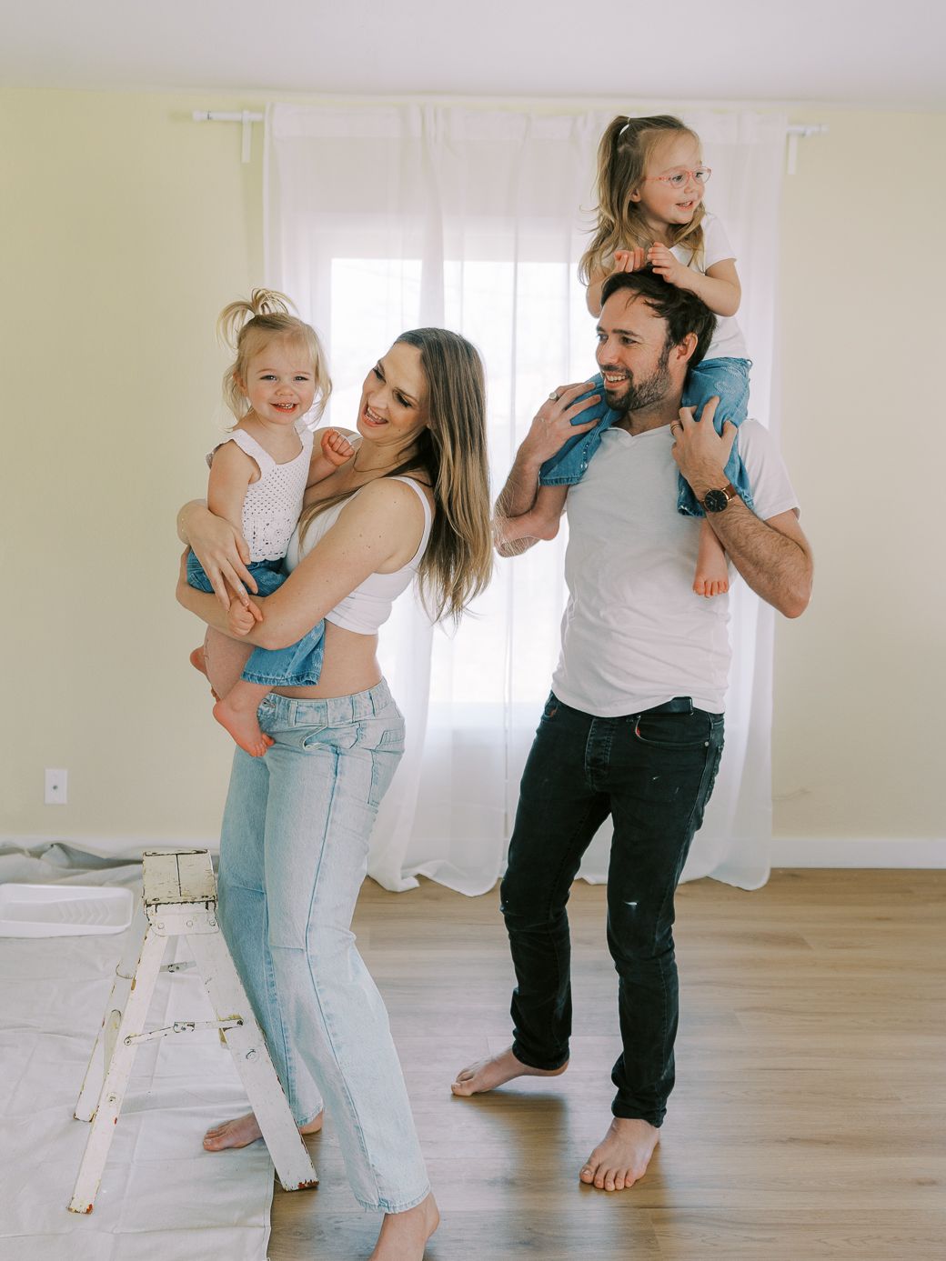 Family playing and dancing together in a bright sunlit room with hardwood floors.