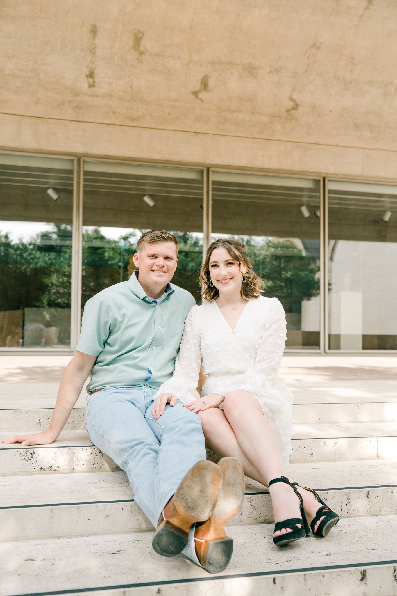 Couple sitting casually on concrete steps during engagement photo session.