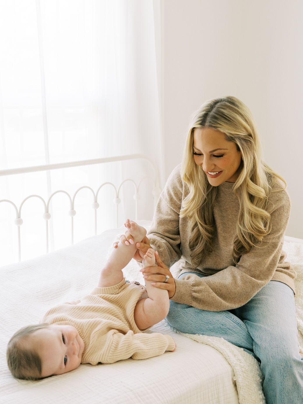 Mother and baby sharing joyful moments together on white bedding in sunlit room.