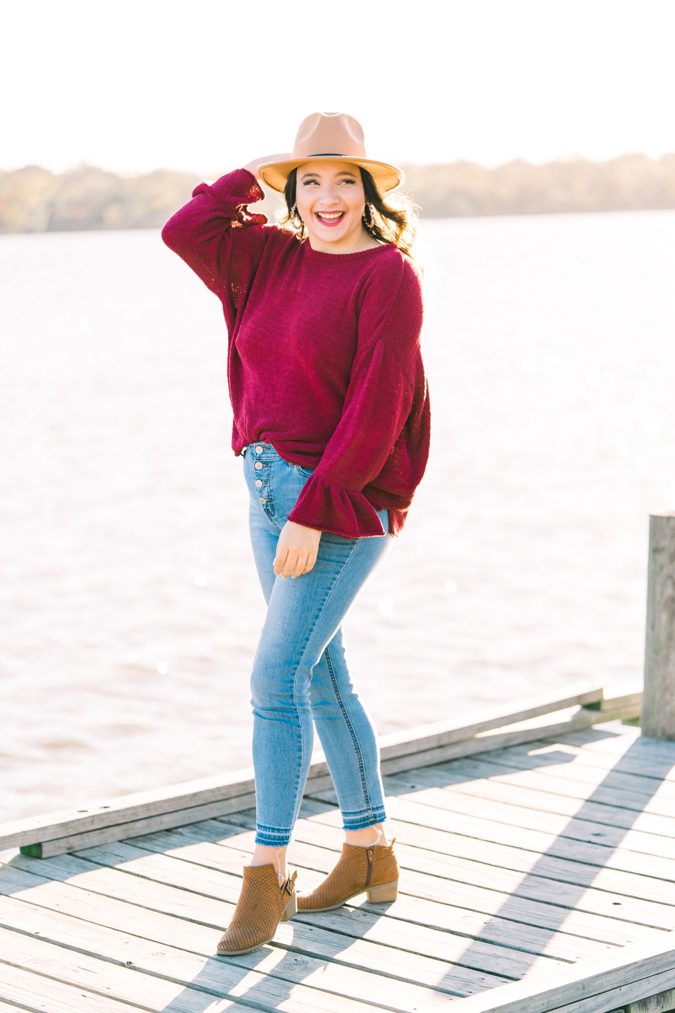 Trendy fall outfit with oversized burgundy sweater and light wash denim photographed at sunset.