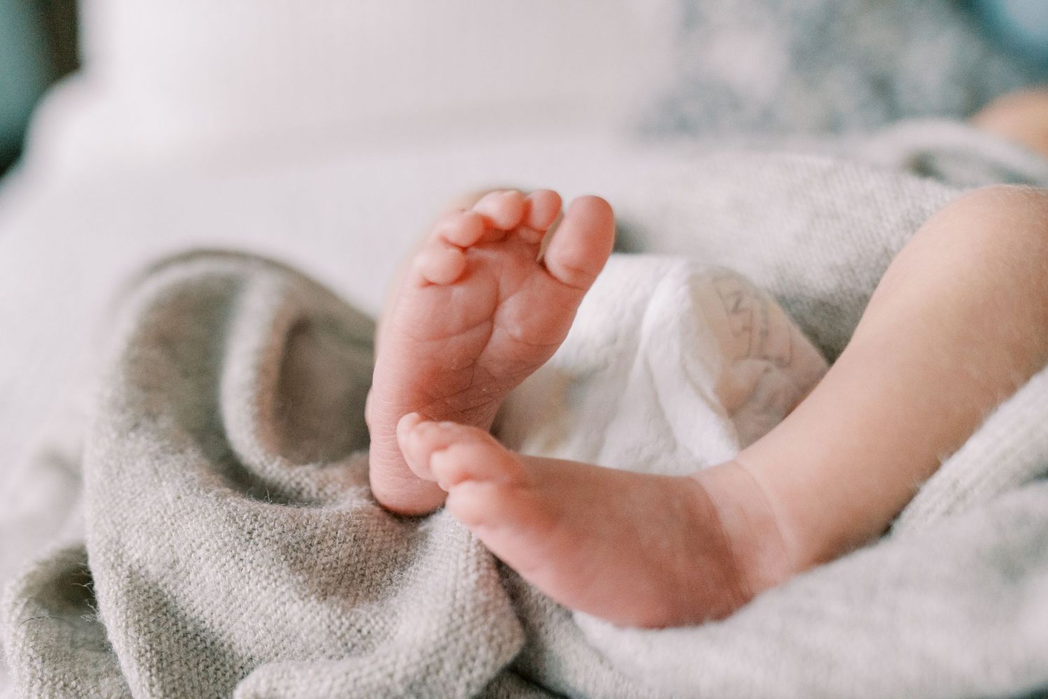 Detail shots of baby's tiny feet and hands against soft gray fabric.