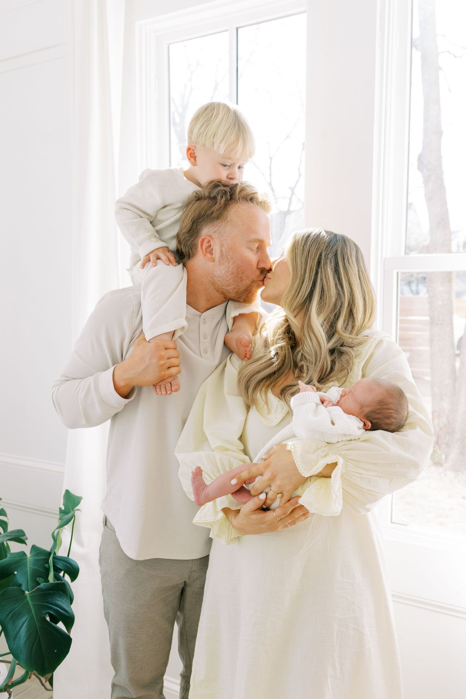 Family in white clothing shares tender moments together in a bright sunlit room.