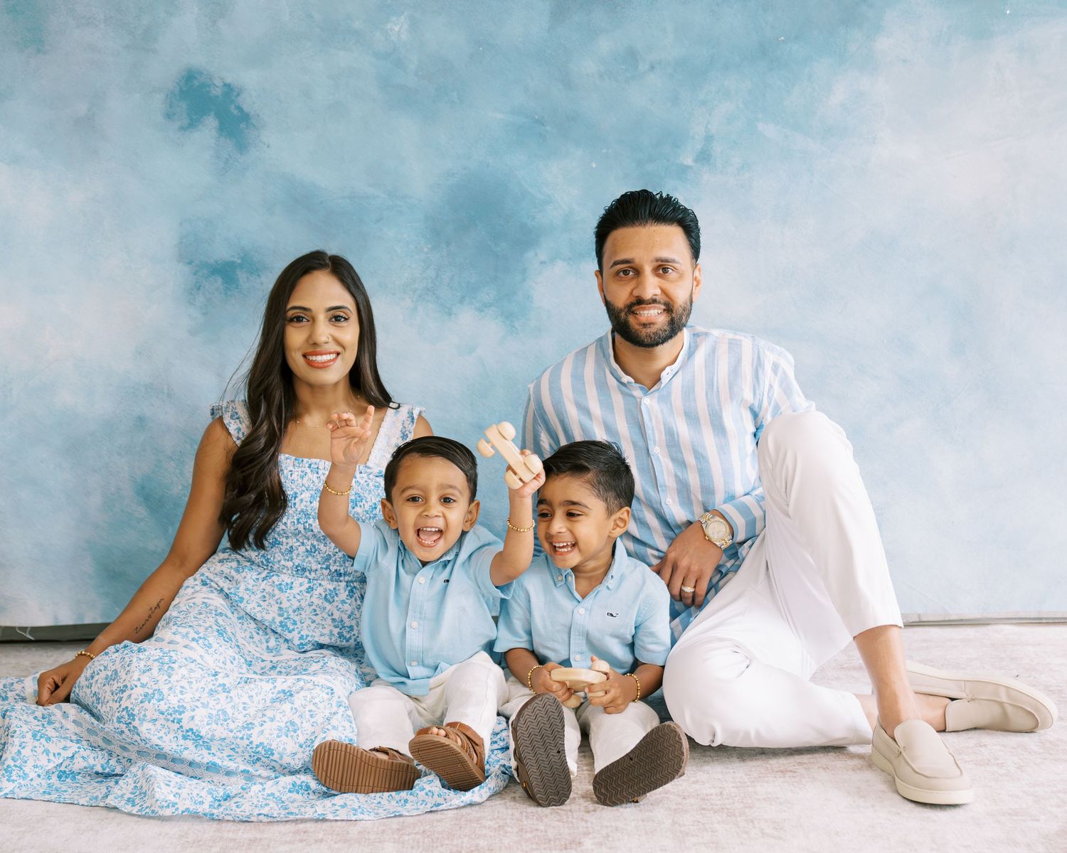 Family of four poses together smiling in coordinating blue and white outfits against a blue backdrop.