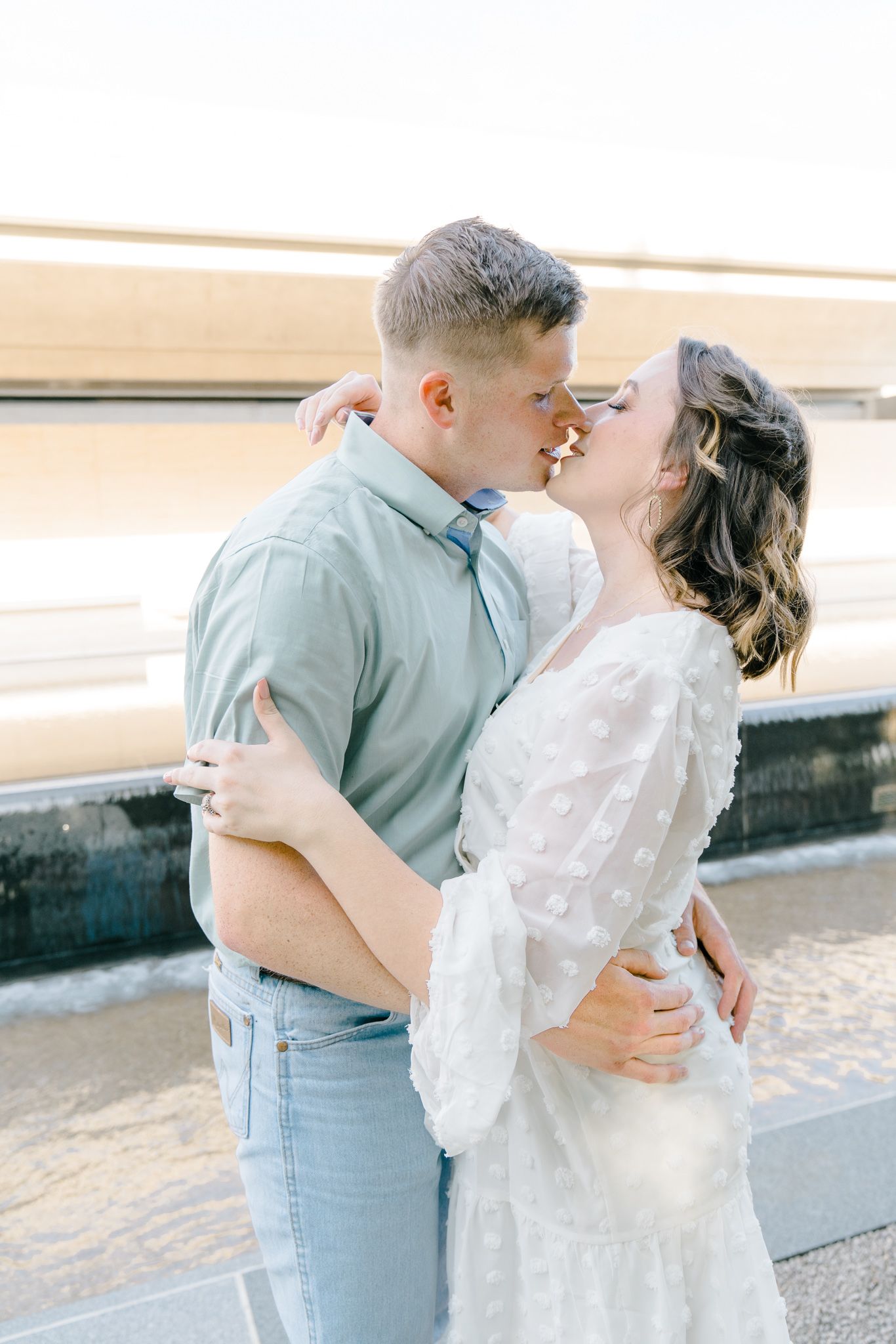A romantic couple embraces in soft lighting wearing coordinating blue and white outfits.