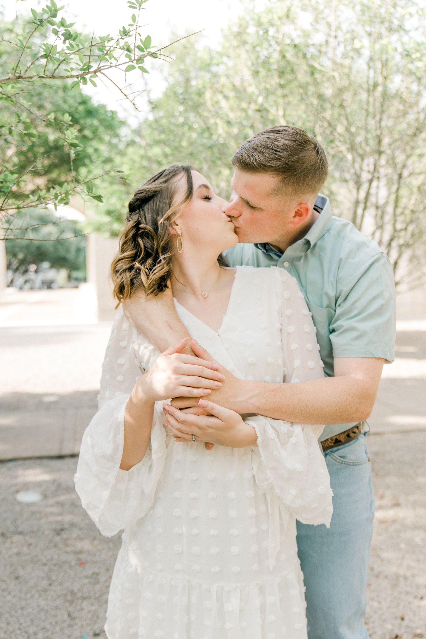 Romantic couple in a white dress and mint shirt share tender moments in a sunlit wooded area.