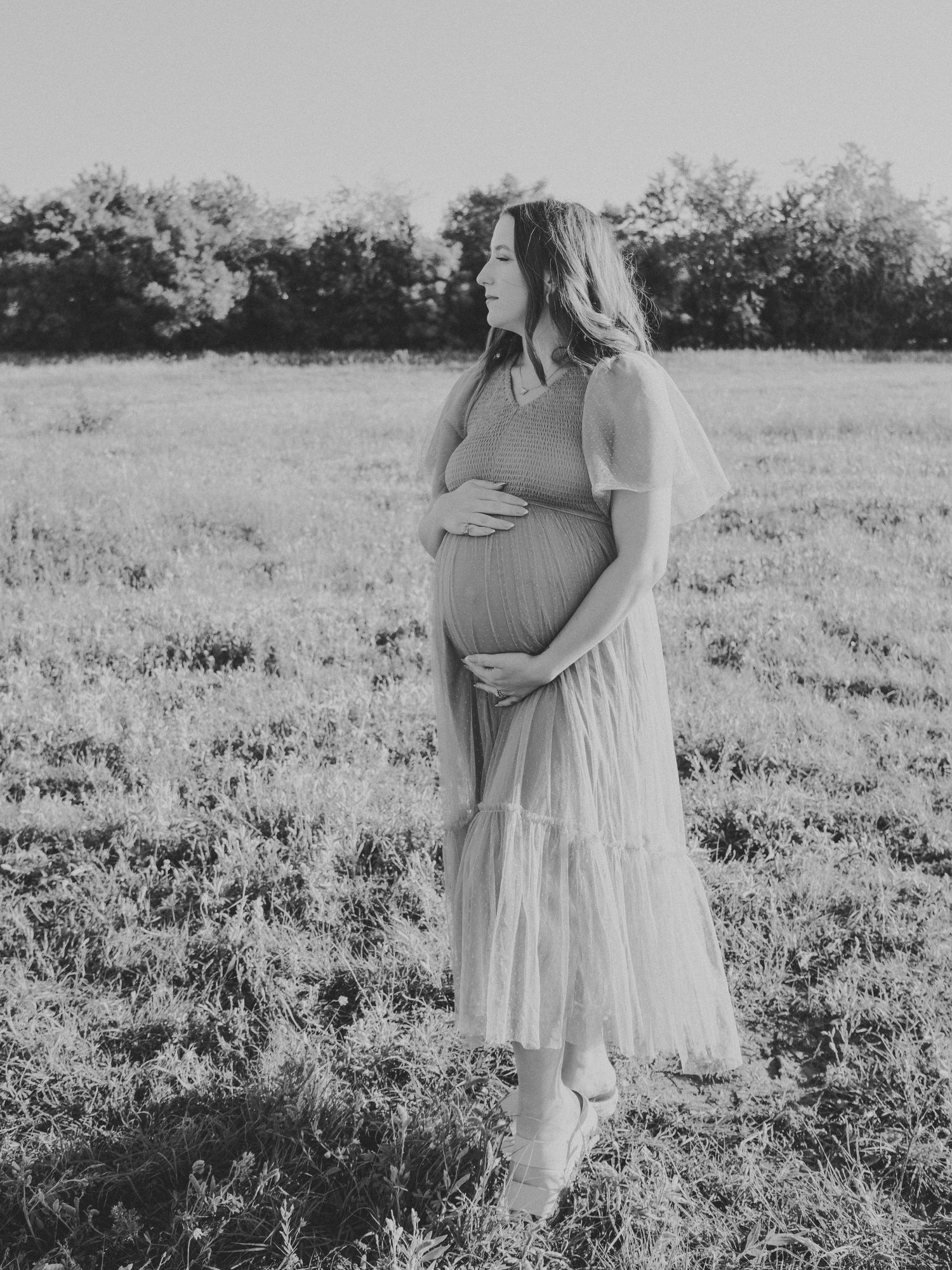 A maternity photoshoot in black and white shows a couple embracing in a wildflower field.
