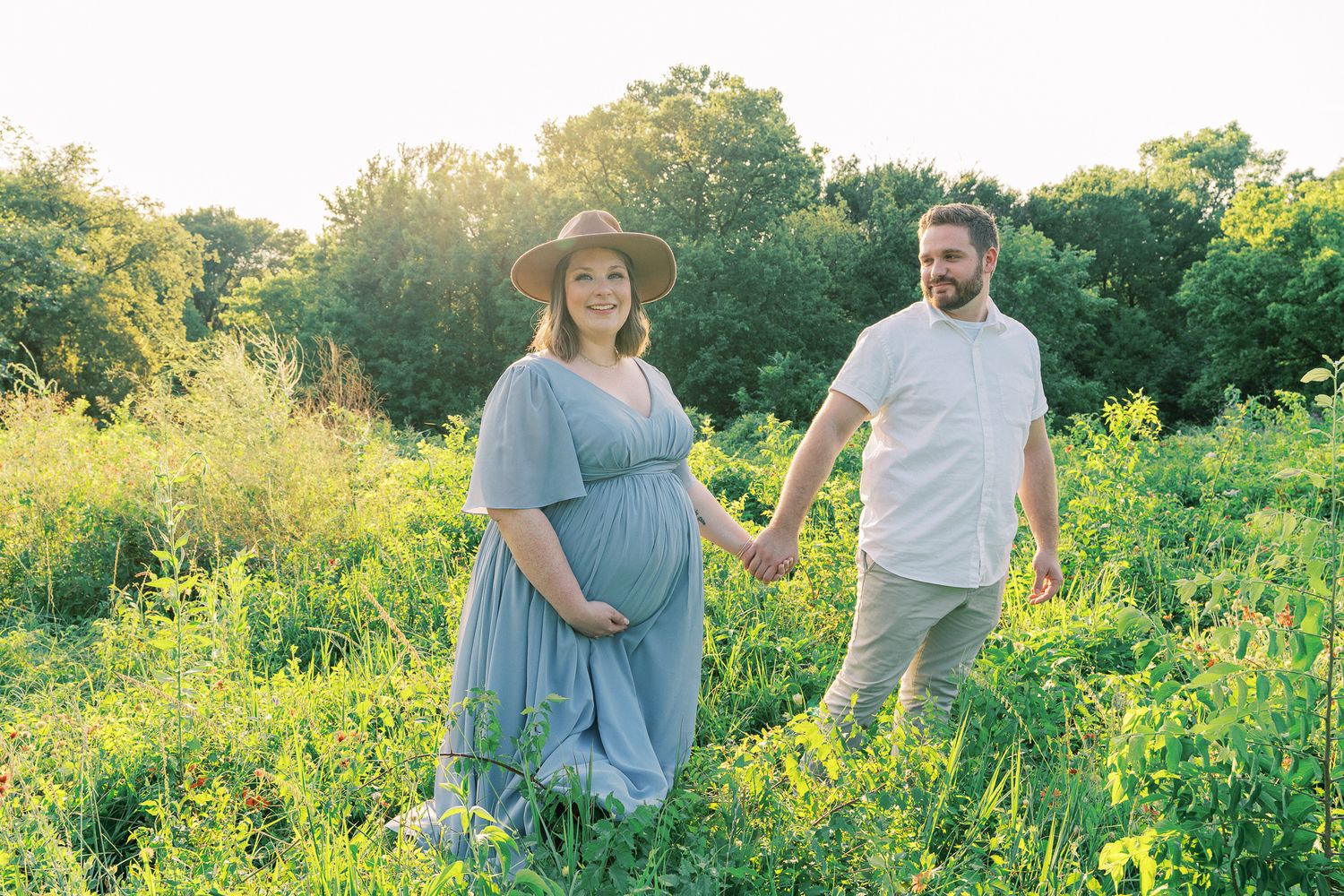A couple embraces in a sunlit meadow filled with wildflowers during golden hour.