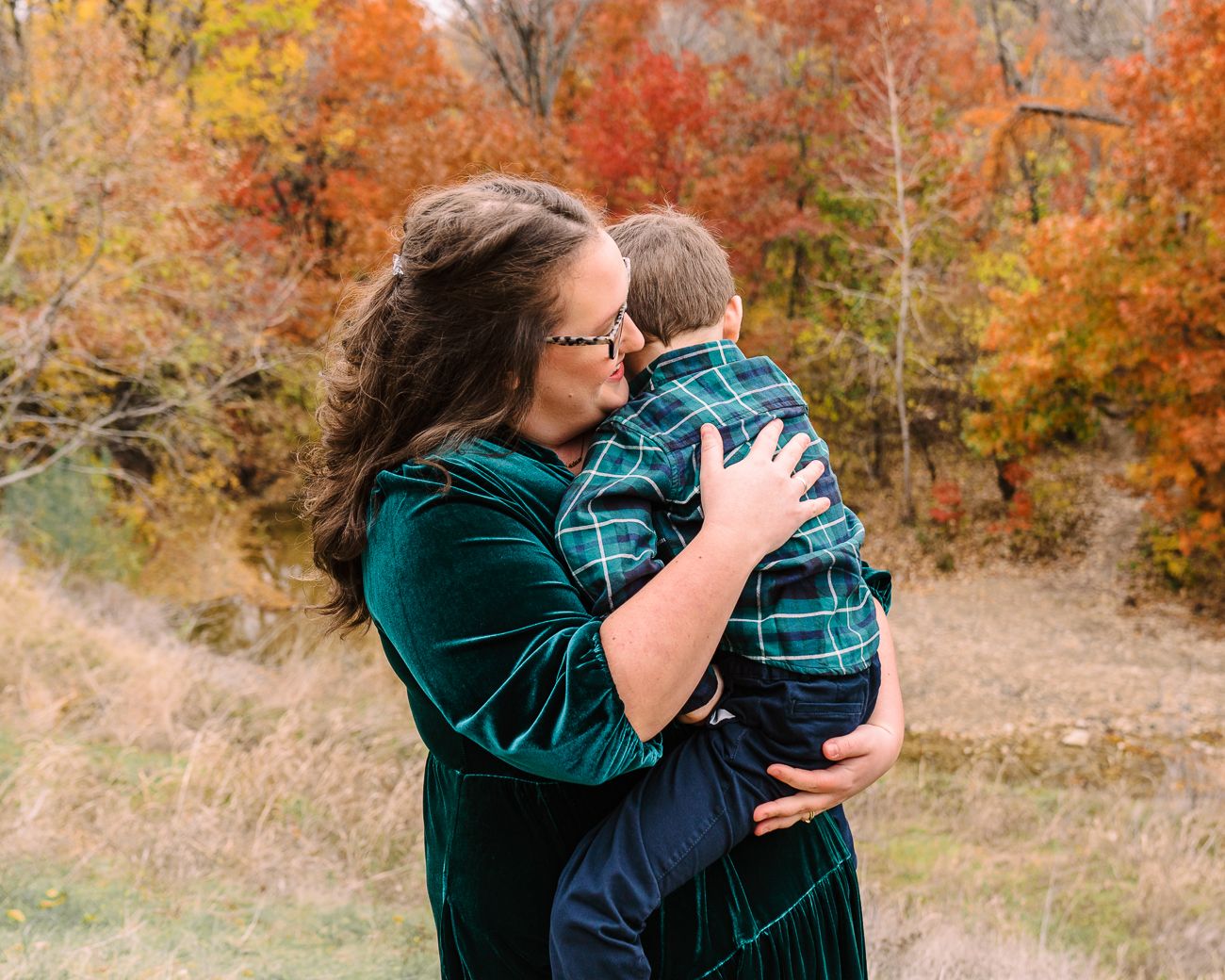 Two people share an intimate embrace surrounded by vibrant autumn foliage in a natural outdoor setting.