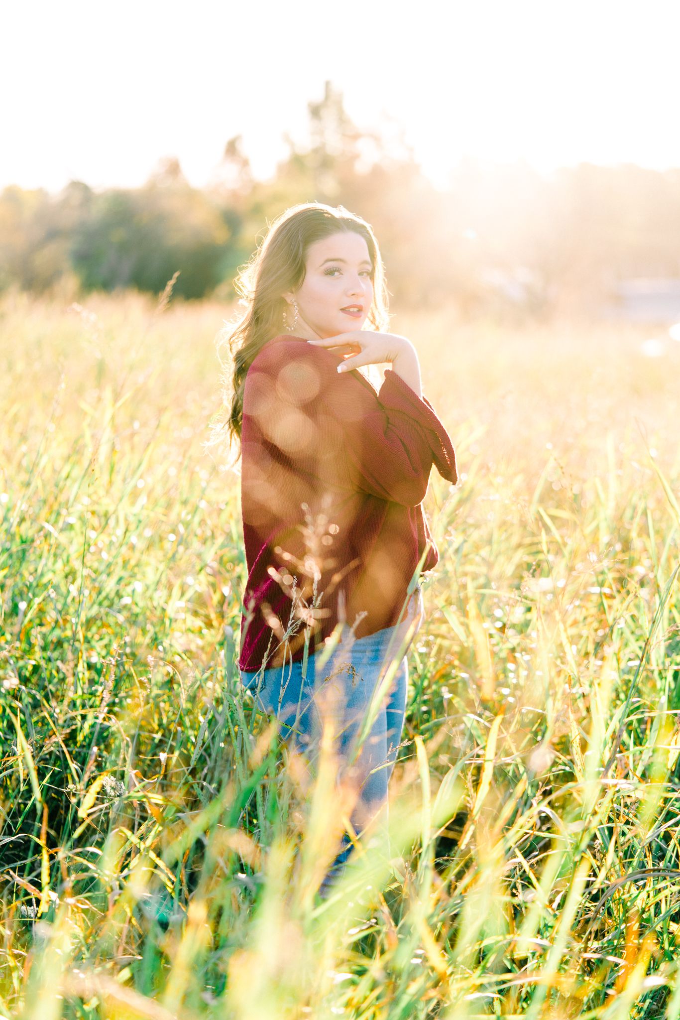 Person in red sweater dancing through tall grass with sunlight creating a dreamy golden glow.