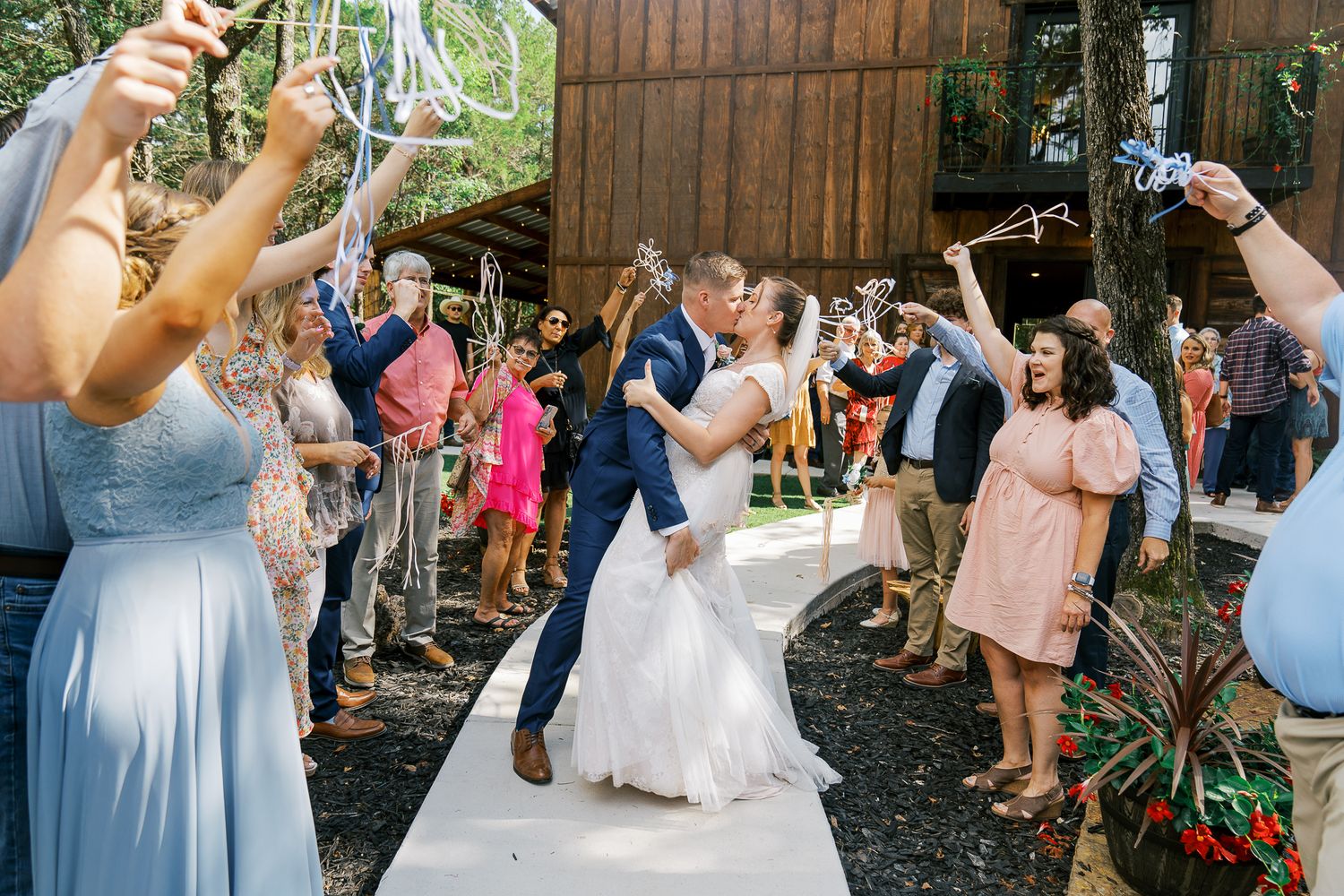 Wedding party members dancing and celebrating together at an outdoor reception venue with rustic wooden decor.