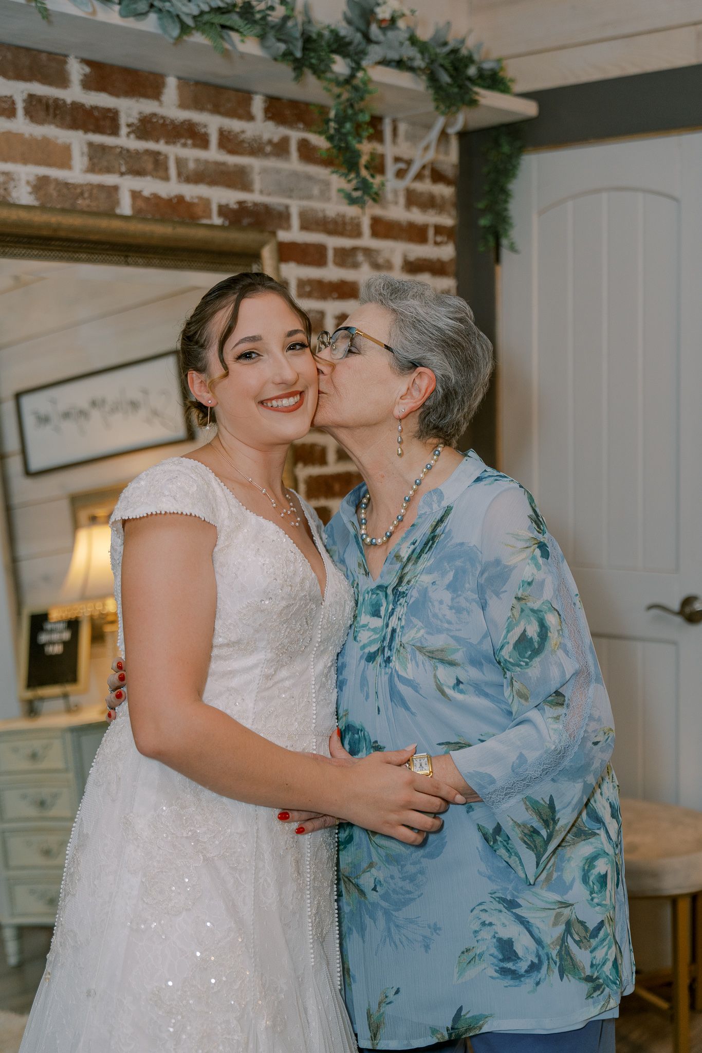 A tender moment shared between two people wearing white and blue floral attire in a rustic brick interior setting.