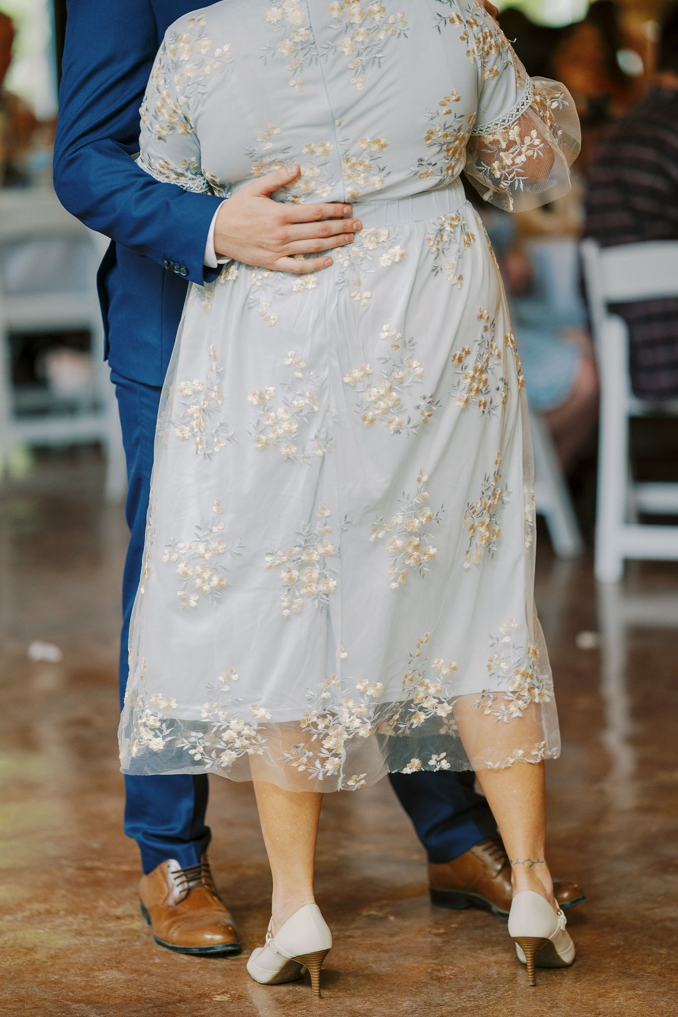 Close-up view of bride and groom's feet showing contrasting footwear with white bridal shoes and brown leather dress shoes.