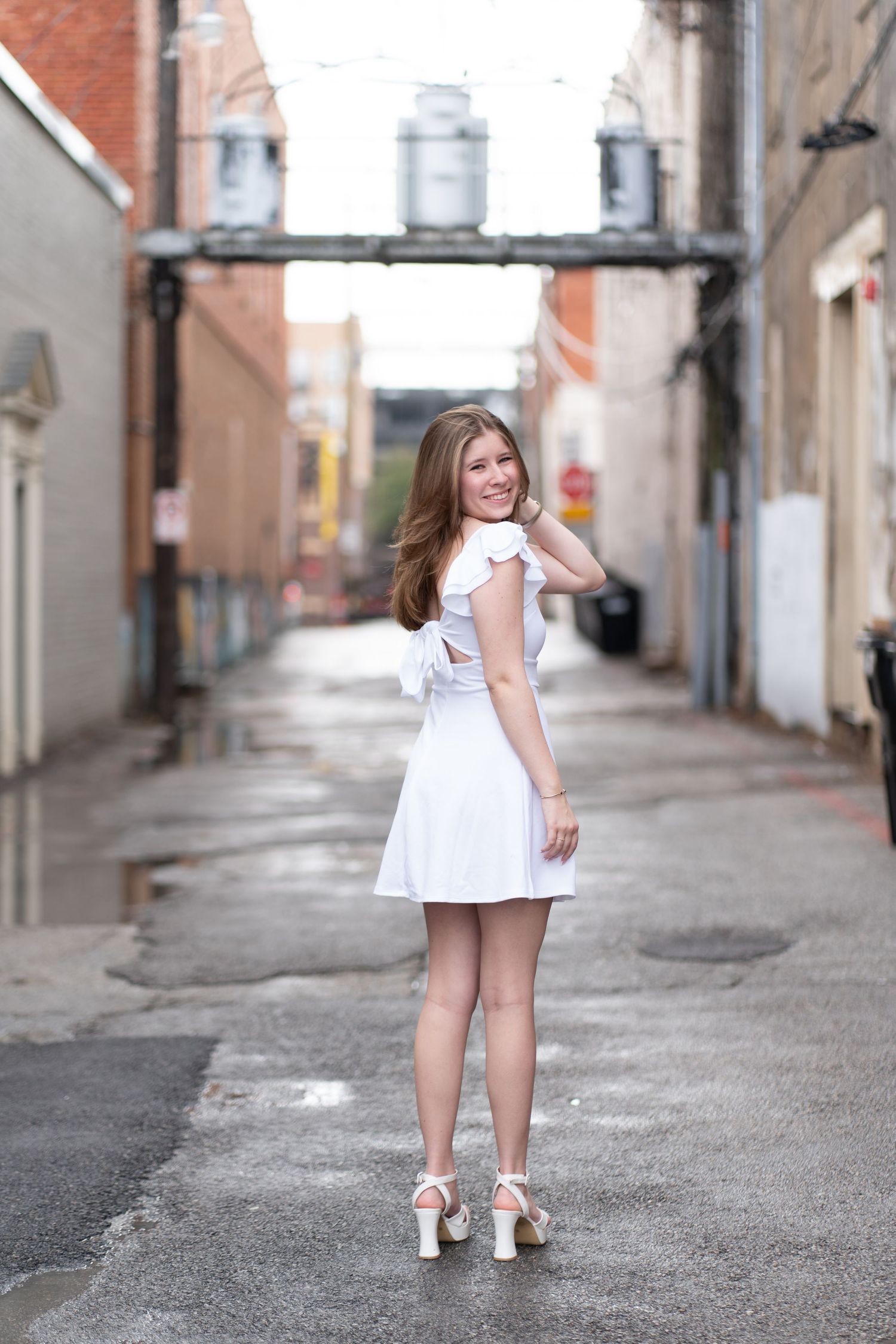 A child in a white dress stands in an alley while looking back over their shoulder in a sequence of four photos.